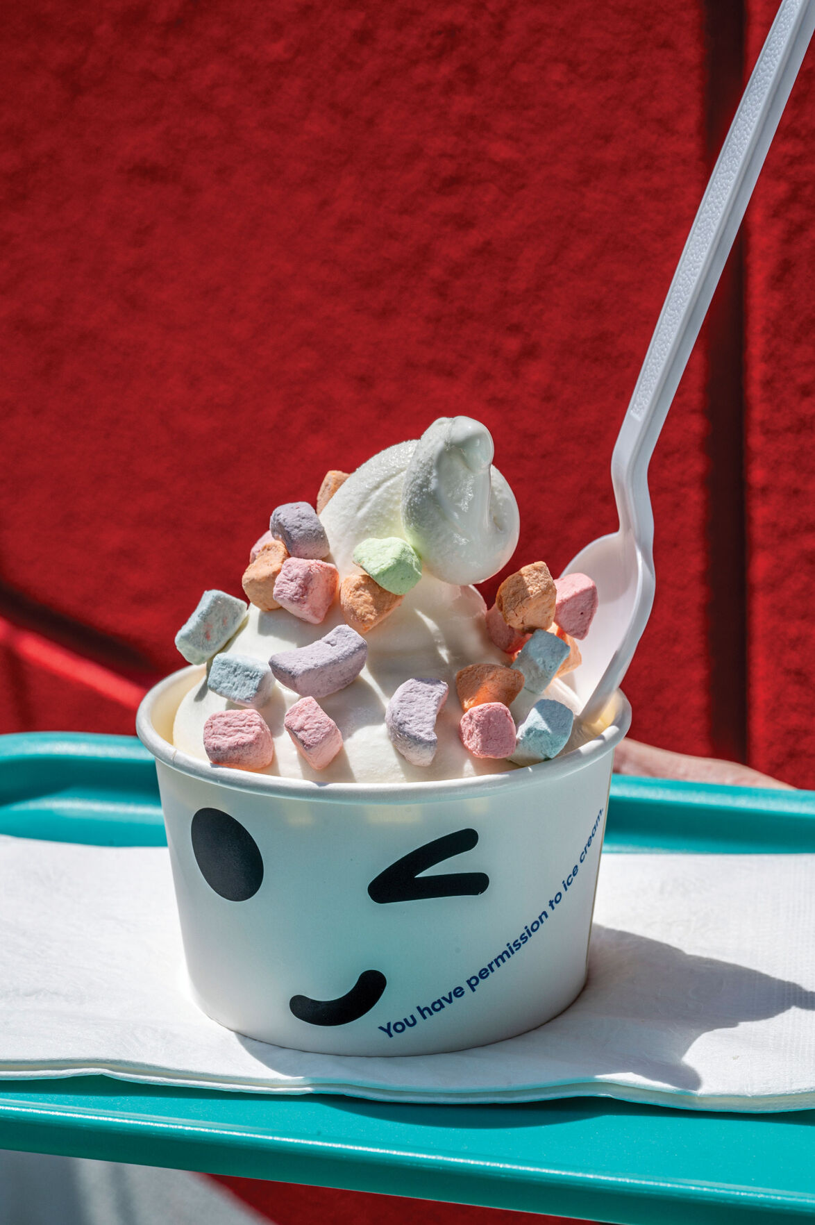 A scoop of ice cream topped with marshmallows in a cup featuring a winking smiley face